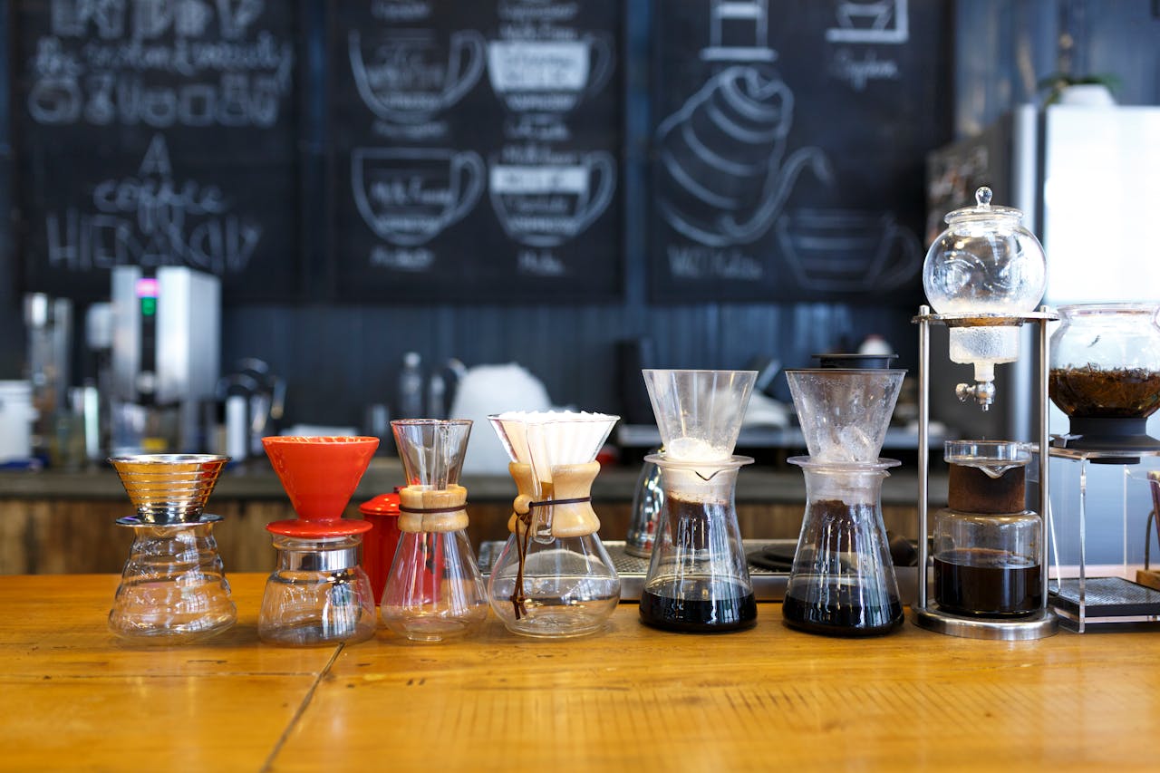 Selection of pour-over coffee makers lined up on a wooden counter in a cozy cafe setting.