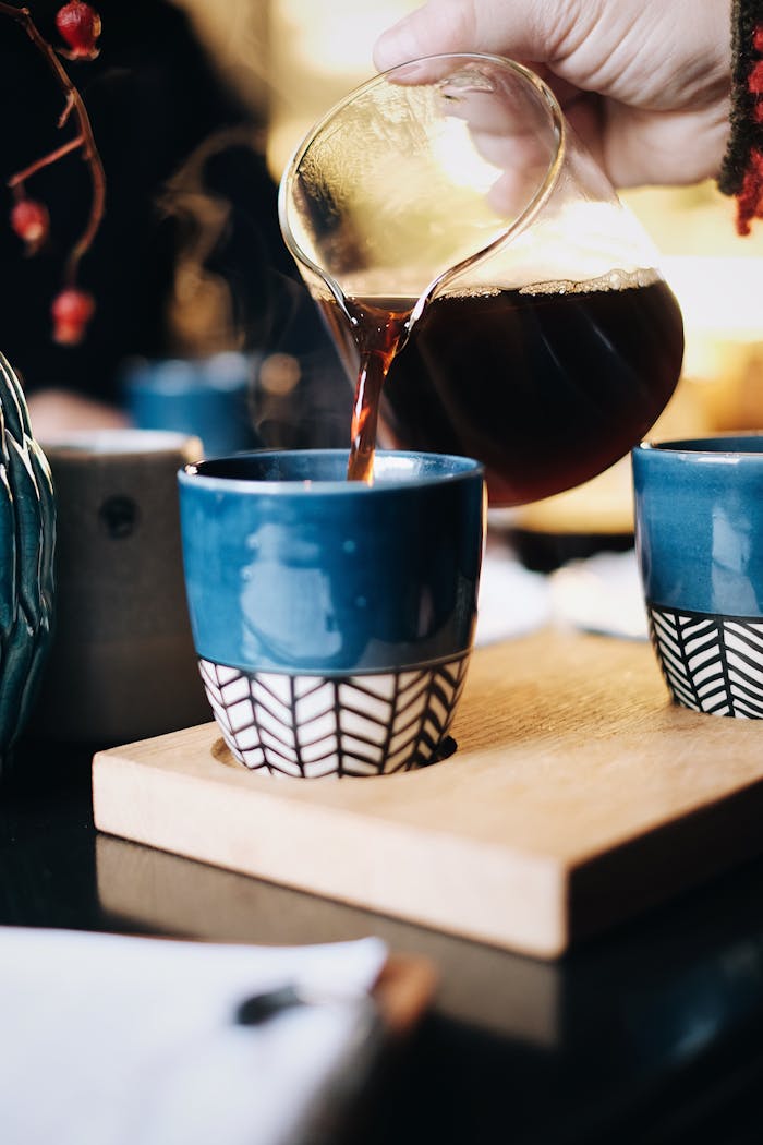 Hand pouring hot coffee into a blue ceramic cup, creating a cozy indoor vibe.